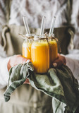 Immune boosting vitamin health defending drink. Woman bottles with fresh turmeric, ginger and citrus juice shots in hands, selective focus. Pure vegan Immunity system booster