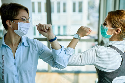 Business colleagues with face masks greeting with elbows during coronavirus pandemic.