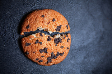 One broken cookie in two pieces, with chocolate on a black background. Image for an inscription.