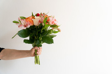 Bouquet of beautiful flowers in mans hand on white background. Minimalistic concept. Space for text.