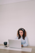 © NatRomero - Pretty woman is sitting in front of her laptop and writes something on the keyboard. She has a cup of coffee and his cell phone next to her. While he writes he is smiling.