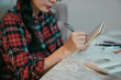 © PR Image Factory - closeup view of woman's hand holding pen jotting down on notebook. girl sitting by table with workbook keeping track of spending with the help of calculator.