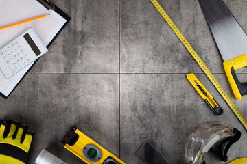 Contractor concept. Tool kit of the contractor: yellow hardhat, libella, hand saw. Plans and notebook on the gray tiles background.