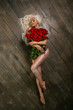 Young sexy blonde with a huge bouquet of red roses in a silver dress. Portrait of a beautiful girl with flowers on a wooden background. The work of a professional makeup artist