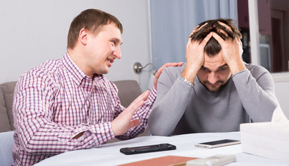 Wall Mural - Friend soothing upset man at home table