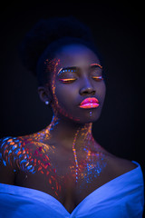 Wall Mural - awesome african model in neon light, unusual interesting portrait of beautiful girl with fluorescent makeup on whole body. isolated dark background