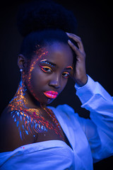 Wall Mural - portrait of beautiful african extraterrestrial model woman in neon light.female with fluorescent make-up, body art design of female posing in UV with colorful make up