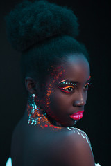 Wall Mural - young and beautiful sensual woman of african appearance in fluorescent paint makeup, posing. luminescence paint, body art, neon lights. isolated