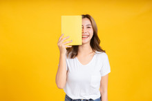 Portrait Young Happy Asian Woman Book Covering Your Eye Reading Education Studying Learning Knowledge Smiling Positive Emotion In White T-shirt, Yellow Background Isolated Studio Shot And Copy Space.