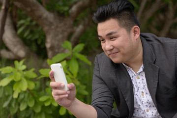 Wall Mural - Young overweight Asian businessman using phone at the park