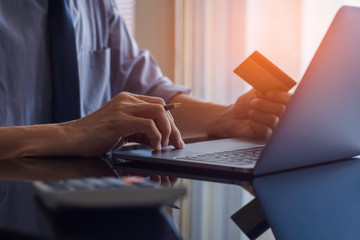 Business man hand work on laptop computer for online payment and digital banking by using credit card with calculator on the table at home office. Online shopping and payment, ecommerce concept.