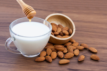 Wall Mural - Closeup glass cup of almond milk with almonds seeds in wooden bowl with honey isolated on wood table background.