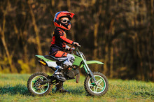 Child On His Small Motorcycle. Small Biker Dressed In A Protective Suit And Helmet. The Kid Is Engaged In Motocross.