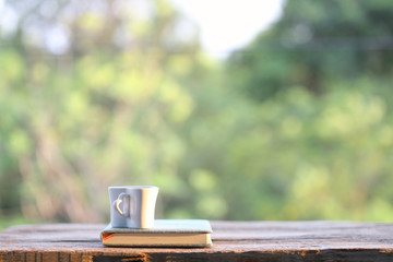 Wall Mural - White cup with notebook on wooden table with nature view