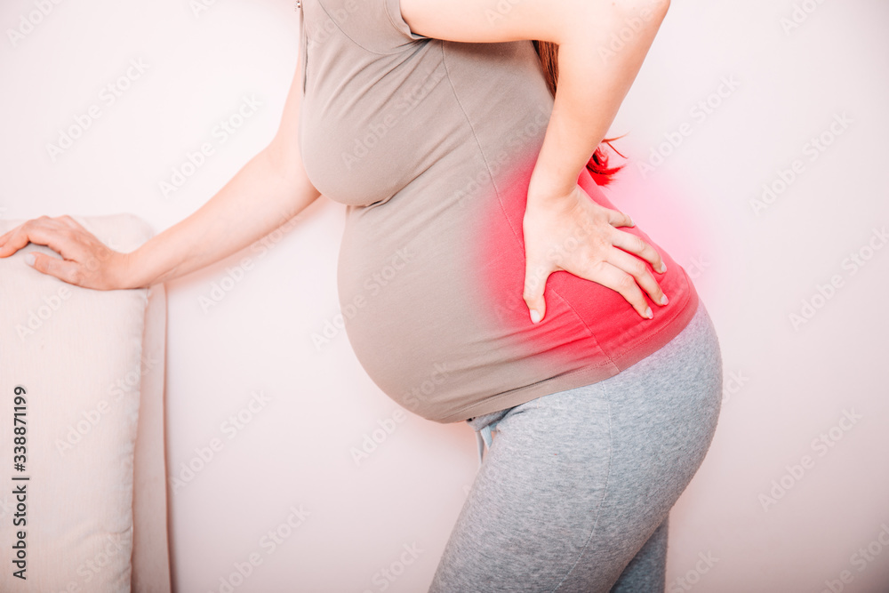 Cropped view of young pregnant woman massaging her back. Horizontal shape, side view, copy space. Torso of pregnant woman with backache, pain in red. - obrazy, fototapety, plakaty 