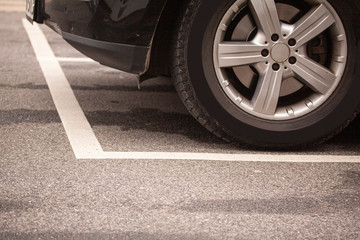 Close up of tyres car wheel from car parking inside white stipes at parking lot on asphalt.