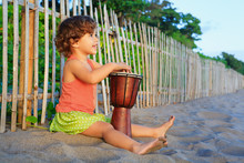 Little Happy Baby Girl Play Ethnic Music On Traditional African Hand Drum Djembe, Enjoying Sunset On Ocean Beach. Children Healthy Lifestyle. Travel, Family Activity On Tropical Island Summer Holiday.
