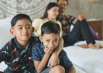 Southeast Asian family spending time at home. Happy Indonesian parents and children laying in bed having fun together