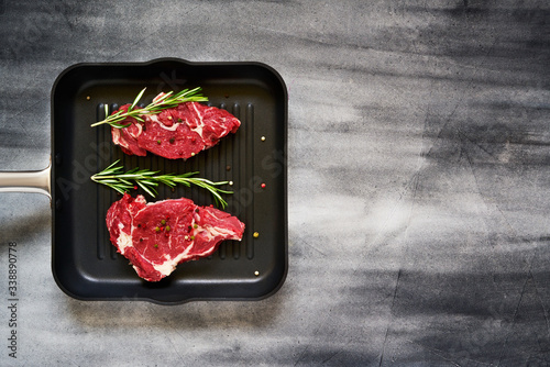 Two fresh raw beef steaks with rosemary and pepper in pan on gray concrete background Canvas Print