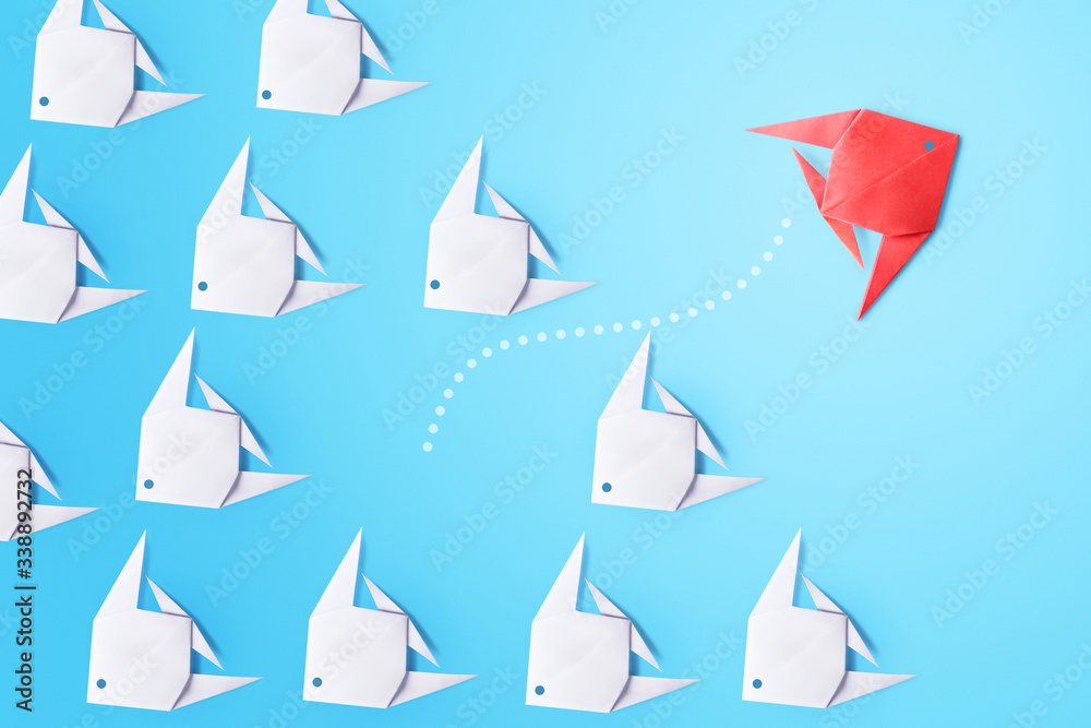 Finding innovative solutions and creative ideas, being unique, thinking different concept. Group of white paper fishes and one red pointing in different direction on blue background - obrazy, fototapety, plakaty 