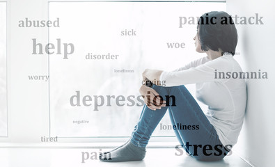 Consequences of depression. Close-up photo of a sorrowful woman who is suffering from stress and claustrophobia, hugging her knees while sitting on a windowsill. Double exposure.