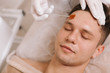 © mad_production - Young attractive man relaxing at spa center while beautician applying peeling lotion on his forehead