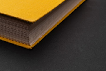 Yellow book on a matte black background. Binding of the book closeup. The book is on the left side of the frame. Copy space