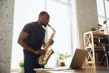 African-american Musician Playing Saxophone During Online Concert At Home Isolated And Quarantined. Using Camera, Laptop, Streaming, Recording Courses. Concept Of Art, Support, Music, Hobby, Education