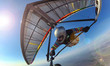 Hang glider pilot on colorful wing makes photo selfie high above ground.