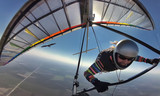 Hang glider pilot on colorful wing flies together with eagle.