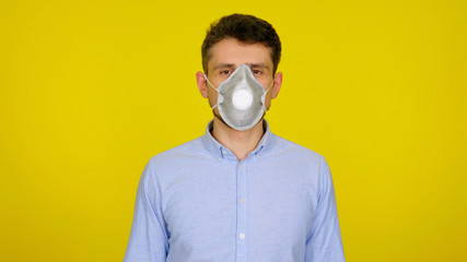 Man in protective respiratory mask looks at the camera. The guy in the blue shirt on a yellow background. Concept against the virus: Coronavirus, flu