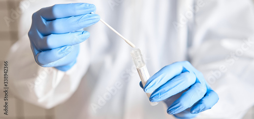 Doctor holding swab test tube for 2019-nCoV analyzing. Coronavirus test. Blue medical gloves and protective face mask for protection against covid-19 virus. Coronavirus and pandemic. © malkovkosta