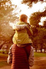 The child sits on his father’s shoulders and walks in the park. Father and baby relationship concept. Active holidays with family