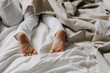 © Bostan Natalia - Toddler boy feet close-up on a bed with white bed sheet, under a blanket. Light white beige tones.