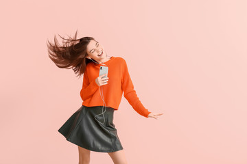 beautiful young woman listening to music and dancing against color background