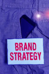 Fototapete - Handwriting text writing Brand Strategy. Conceptual photo Longterm plan for the development of a successful brand Smartphone device inside formal work trousers front pocket near note paper