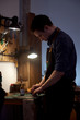 © dneezz - The leather master is working with natural leather at the desk. Vertical photo of the room with wooden table, set of leather craft tools on it and working man. Manufactory and of leatherman.