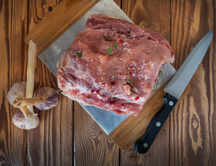 A sore piece of pork loin stuffed with spices for baking on a cutting board and a kitchen knife in a rustic kitchen