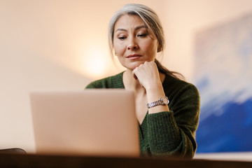 Beautiful grey-haired woman using laptop computer indoors.