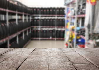 Poster - Empty wooden surface and blurred view of car tires in auto store, closeup. Space for text