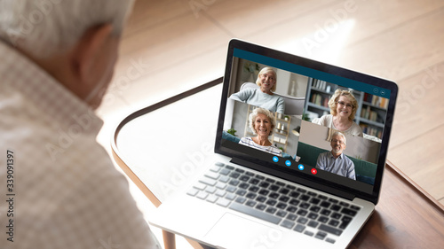 Older generation and modern technologies for virtual visual communication concept. Old man makes videocall talking with relatives or friends by video conference app, pc screen view over male shoulder