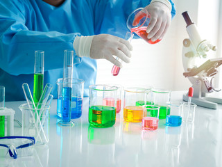 Scientist hand doing science experiment, colorful solutions in scientific glassware on table, researcher working in biology and chemistry laboratory concept