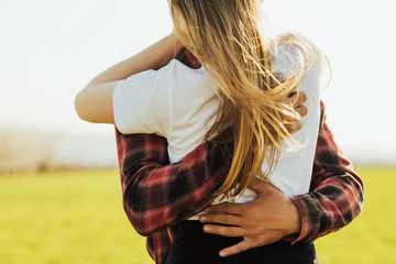 Wall Mural - Cropped shot of young man embracing her  girlfriend from the back at the green field background.  Happiness couple concept. Romantic and togetherness in spring day. Love, trust, romance.