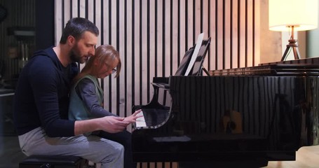 Wall Mural - Dad teaching piano to his daughter.Little girl learning piano at home-Side view.Piano class at home. Child learning piano from her father