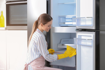 Woman in rubber gloves cleaning refrigerator at home