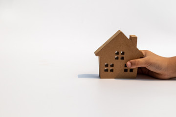 Wall Mural - Child's hand holding small wooden toy house on white background.