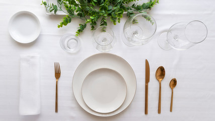 Table setting for elegant festive dinner with white porcelain plates, glasses, decorative textile gold cutlery and center place.