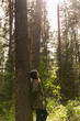 © Eloy - brunette woman with a braid and green jacket leans on the trunk of a forest tree