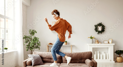 Cuadros en Lienzo Cheerful woman listening to music and dancing on soft couch at home in day off