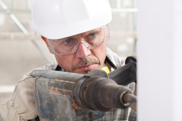 Wall Mural - man using an electric pneumatic drill making a hole in wall, professional construction worker with safety hard hat,, gloves and protective glasses. inside construction site